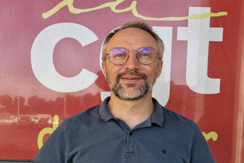 Portrait de Laurent Indrusiak, souriant devant un drapeau de la CGT.