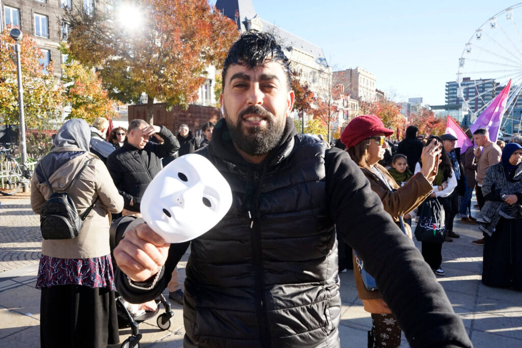 Maachou est au premier plan. Il brandit aussi un masque blanc que l'on vient de lui distribuer. En arrière-plan, on voit quelques manifestants qui commencent à arriver sur la place de Jaude.