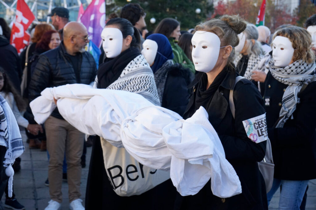 On voit ici la tête du cortège, avec deux personnes portant un masque blanc. Elles portent un drap blanc qui semble rempli d'un cadavre.