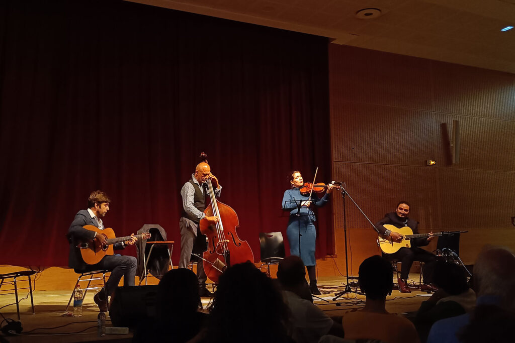 Photo montrant le groupe Les Imposteurs au festival Vichy Jazzy, le vendredi 18 octobre à 20 h 30, à la salle des fêtes de Vichy. Le quatuor est sur scène, en train de jouer son fameux Jazz Manouche devant un public assis face à lui.