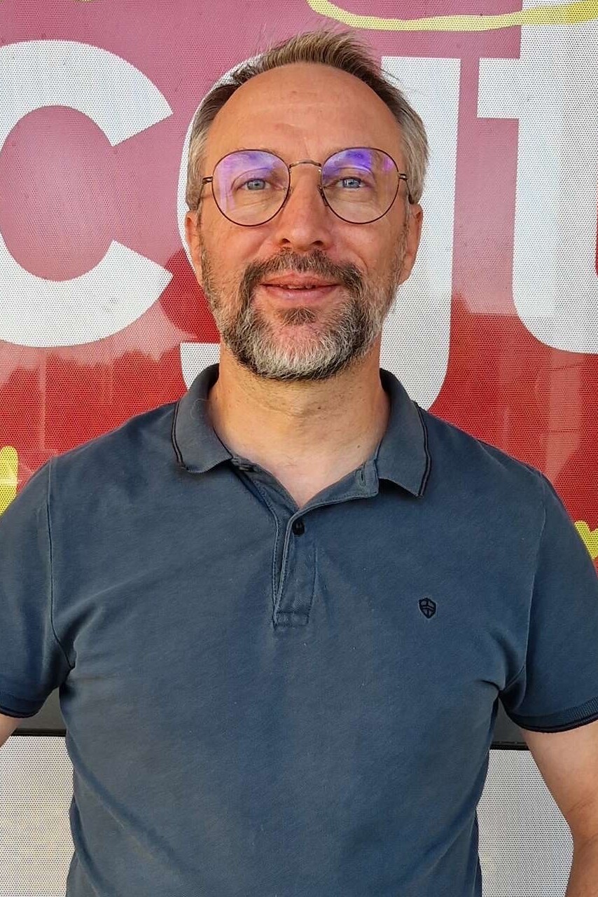 Portrait de Laurent Indrusiak, souriant devant un drapeau de la CGT.