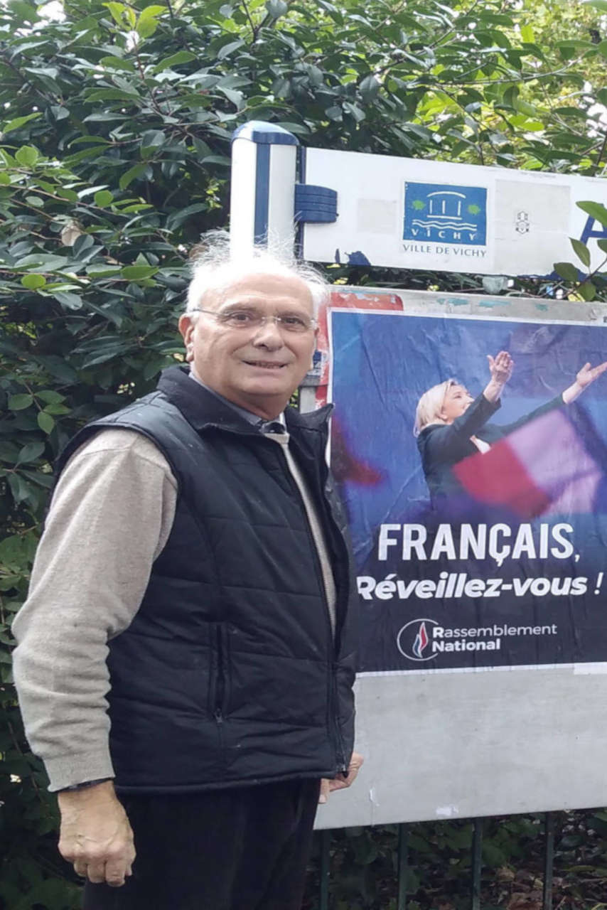 Jean Pierre Sigaud à Vichy pose devant des affiches de campagne RN.